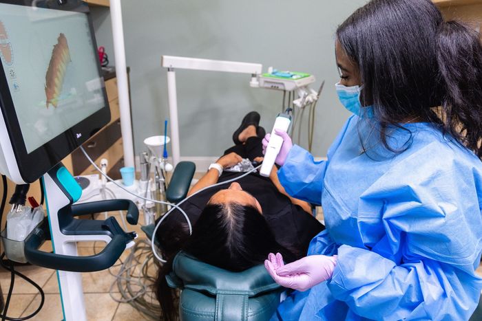 Dentist scanning patient's teeth with digital scanner, showing model on monitor in dental office.