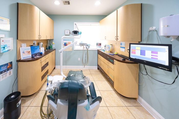 Dental operatory with curved wood cabinets, dental chair, and computer monitor.