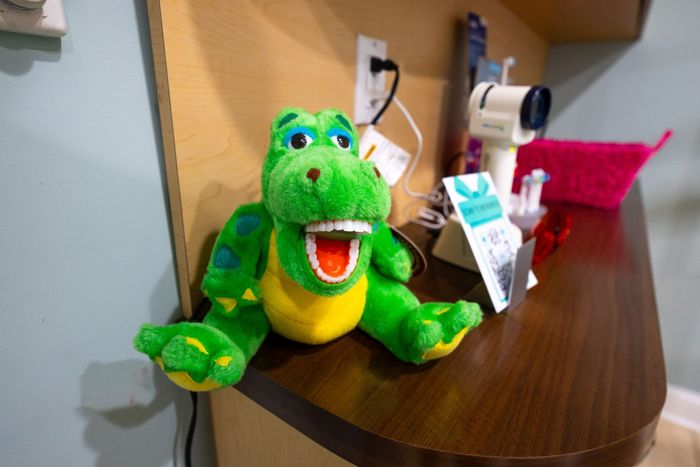 Green plush alligator with open mouth, displaying teeth, on a wood shelf near an electrical outlet.