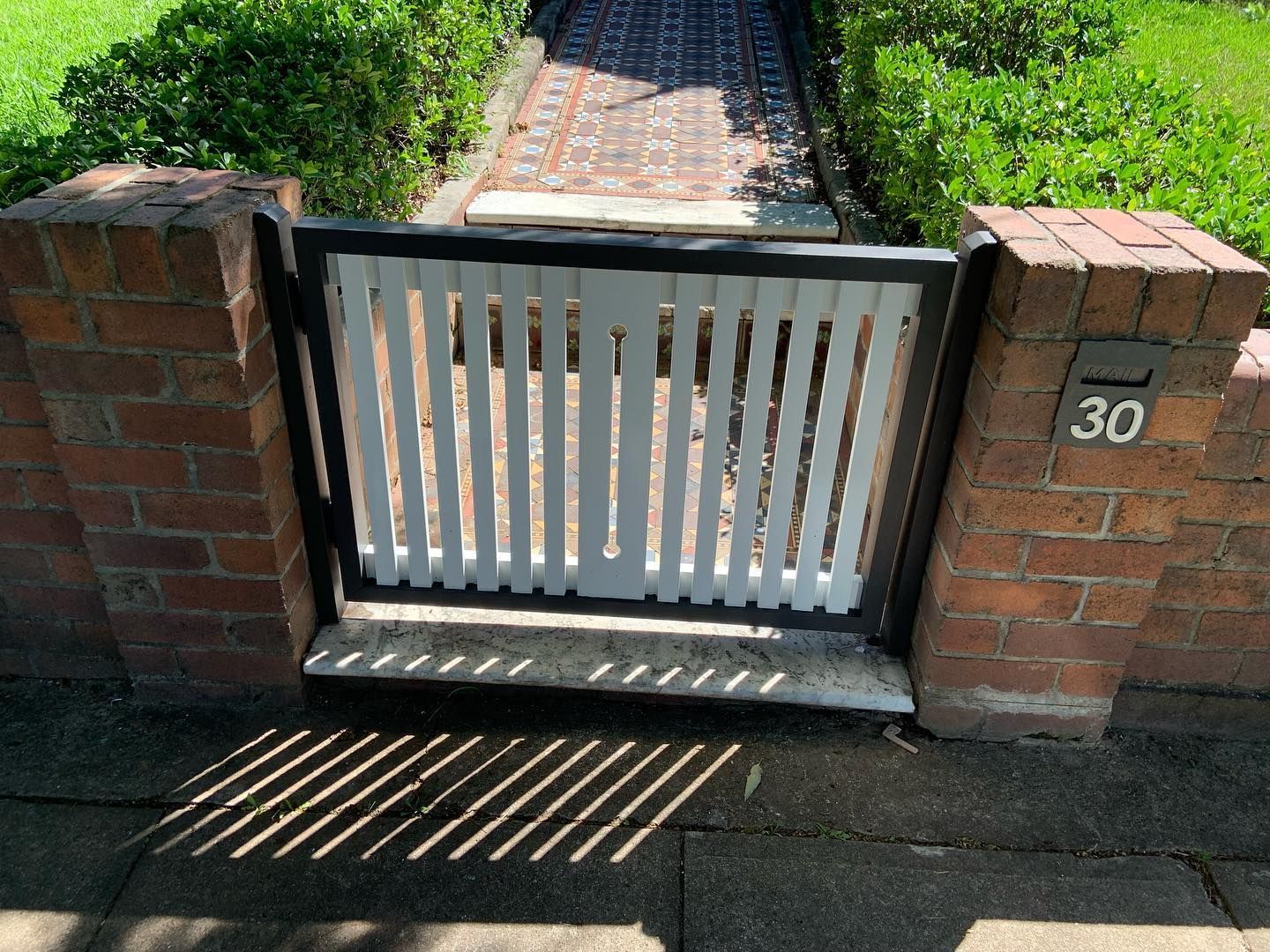 A white, slatted pedestrian gate set in a red brick wall, with the number 30 displayed on the right pillar.