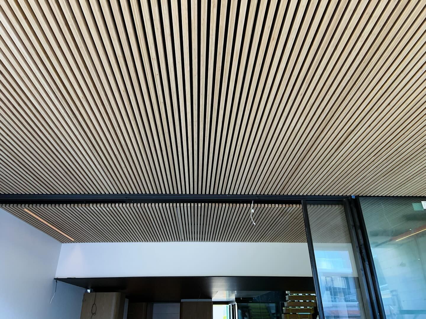 A modern interior ceiling featuring parallel light-wood slats with recessed lighting, seen above a dark framing element.