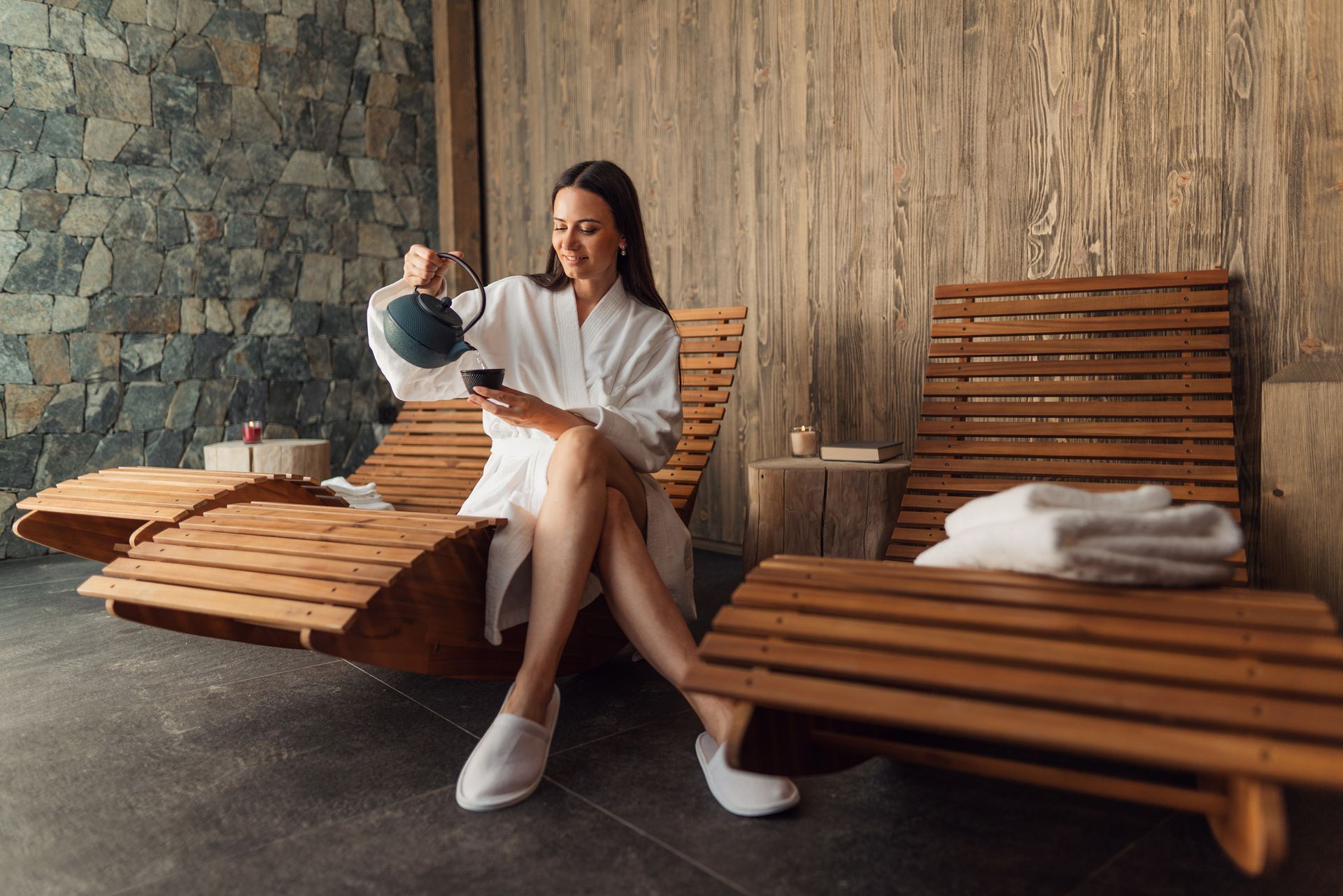 A woman in a bathrobe is sitting on a lounge chair in a spa.