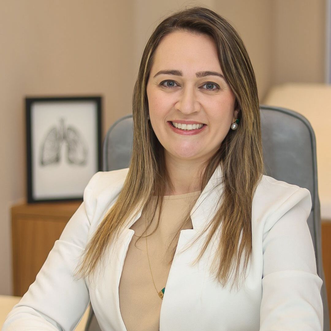 Uma mulher de jaleco branco está sentada à mesa de um escritório.