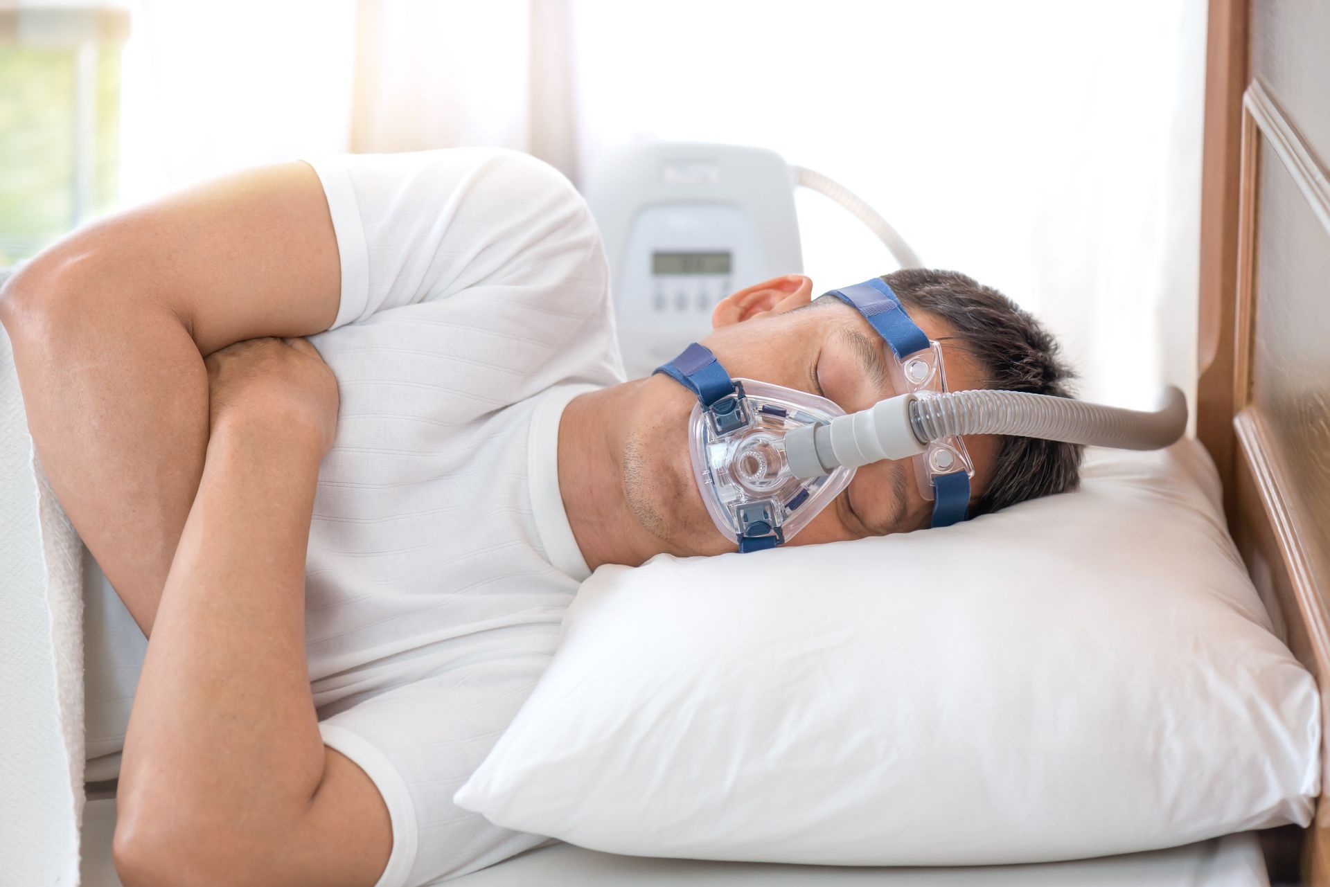 Um homem dorme em uma cama com lençóis e travesseiros brancos.