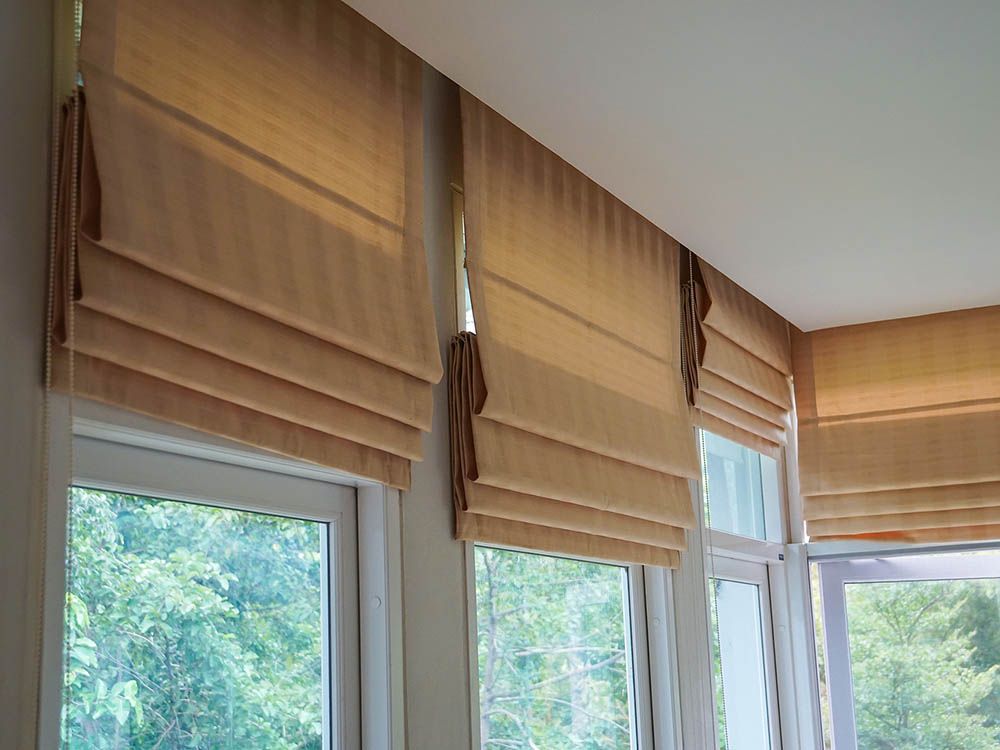 A room with a lot of windows and roman blinds on them.
