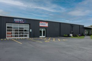 A dark-sided warehouse building featuring Melvin’s Auto Repair, with a glass garage door and front entrance under blue sky.