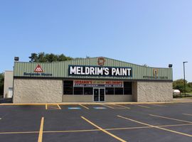 A Meldrim's Paint store with a stone facade and a Benjamin Moore sign under a clear blue sky, seen from a parking lot.