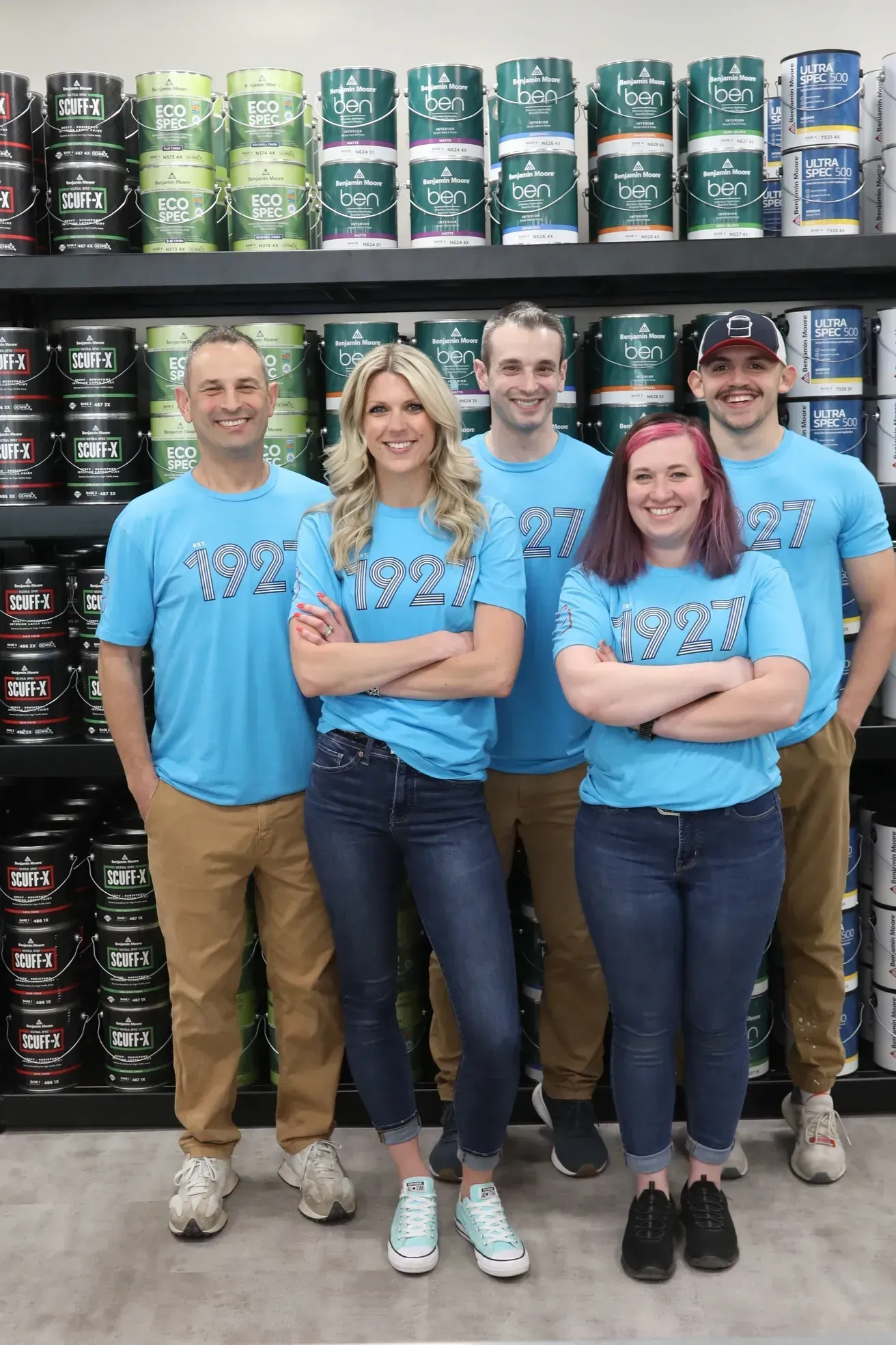 A group of people are posing for a picture in front of a shelf of paint.
