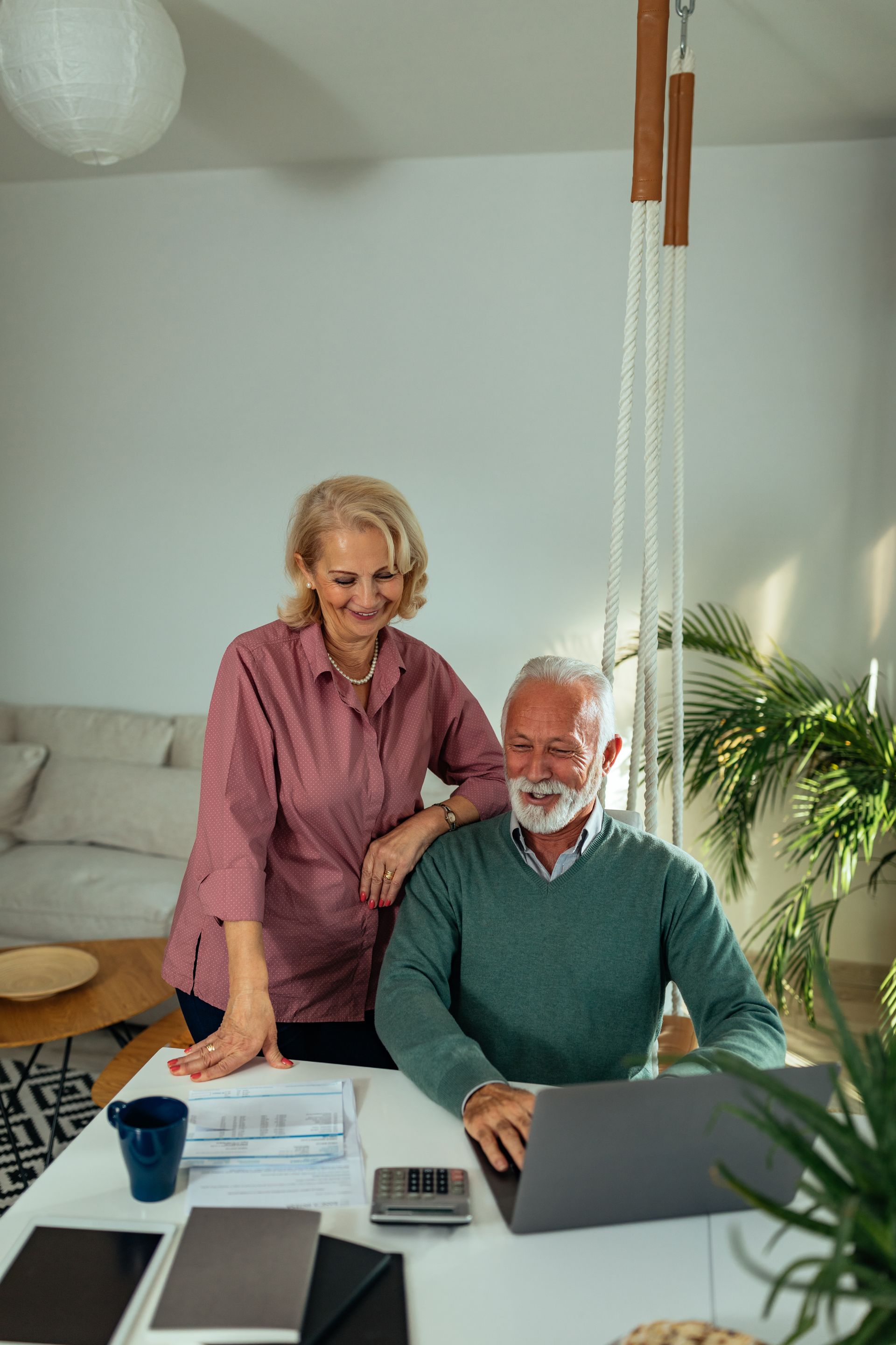 An elderly couple is sitting at a table using a laptop computer.
