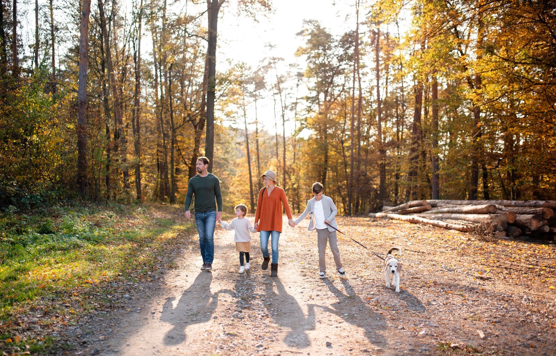 A family is walking down a dirt road in the woods with a dog.