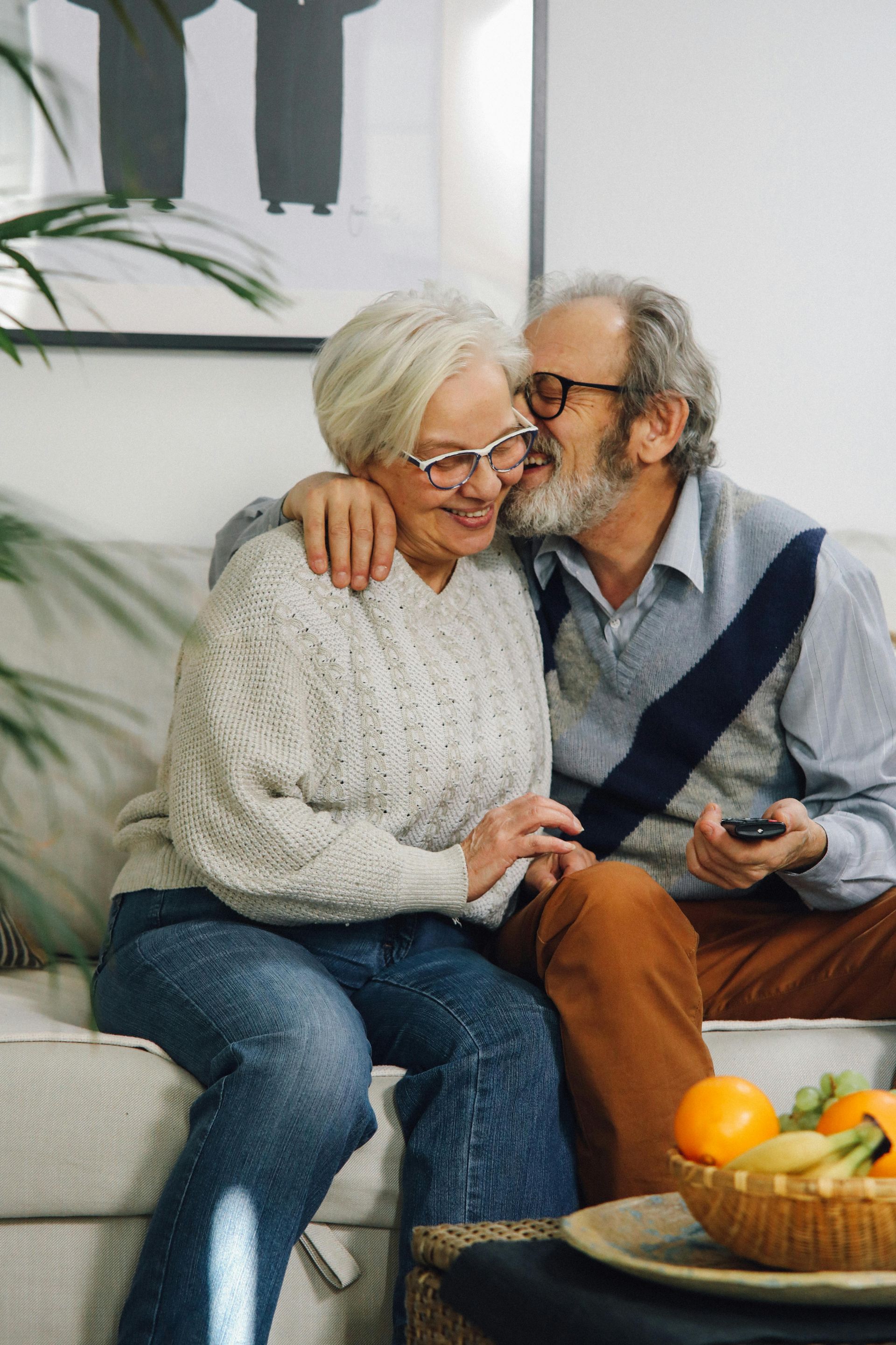 An elderly couple is sitting on a couch and kissing.