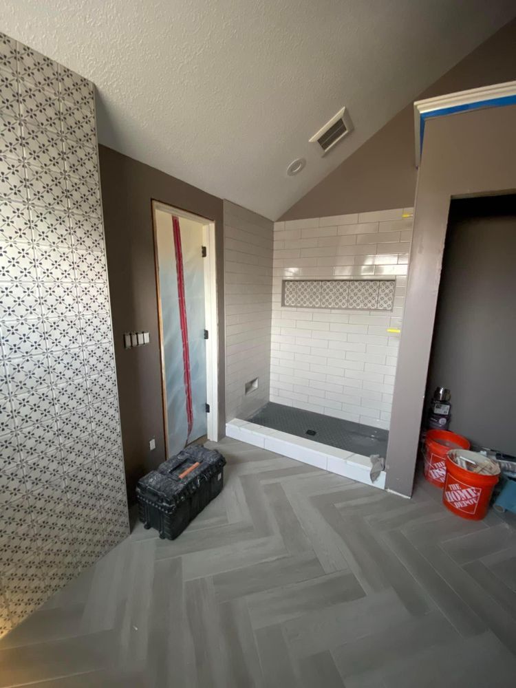 Unfinished bathroom with white tile shower, gray herringbone floor, and tools in a renovation space