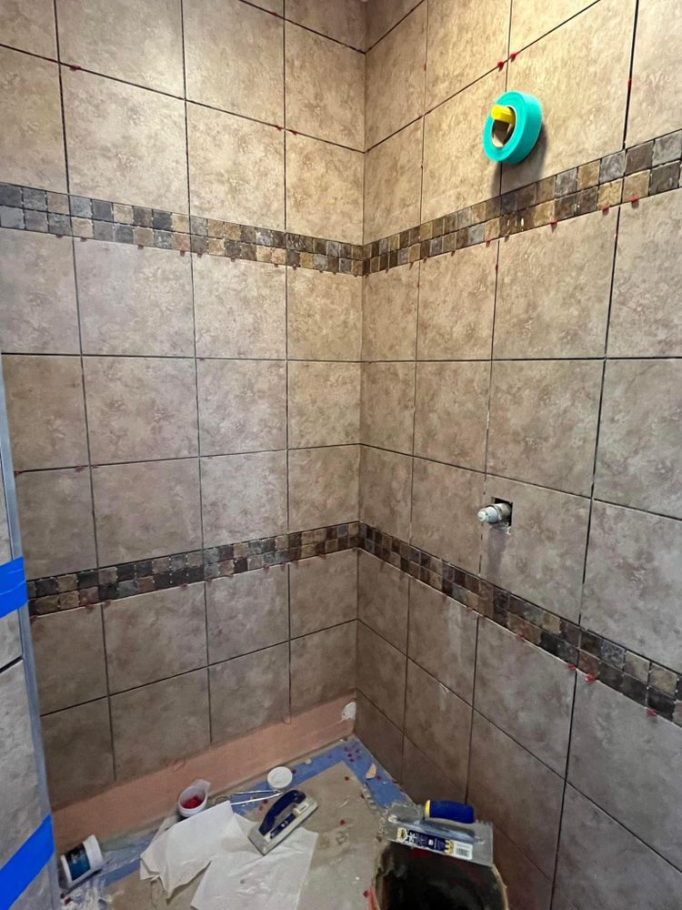 Tiled shower stall with a showerhead, shelves, and cleaning supplies on the floor.