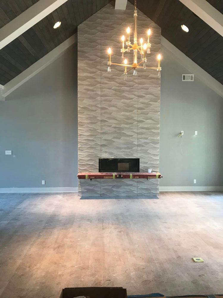 Empty modern living room with vaulted ceiling, chandelier, gray walls, and stone fireplace center.