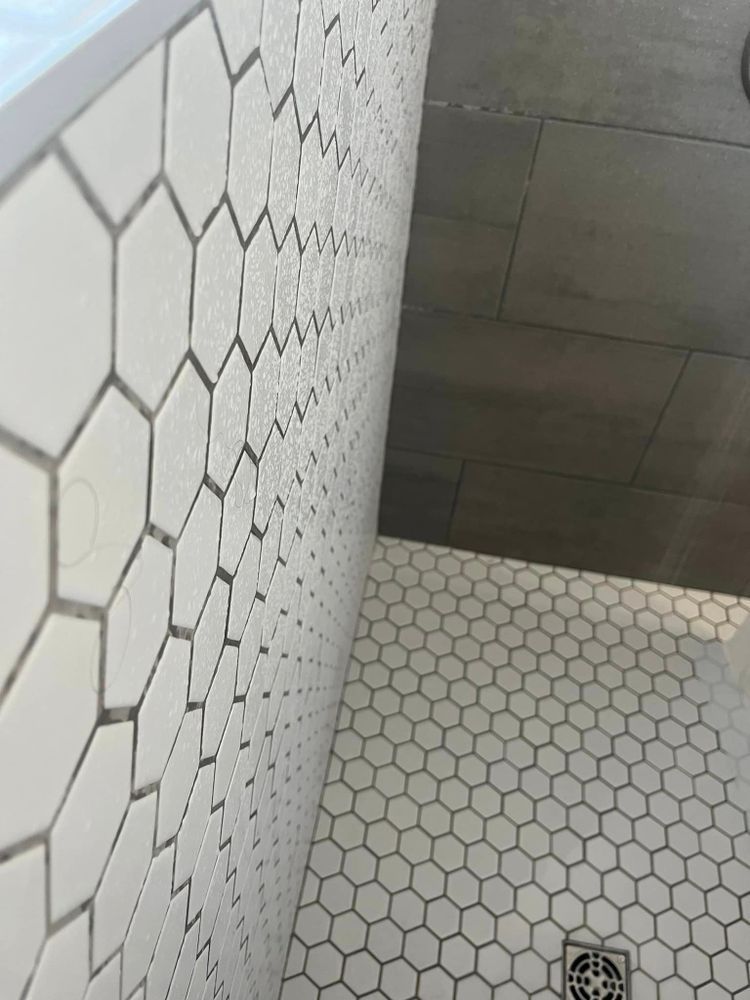 White hexagonal tile wall and floor in a shower area with a drain.