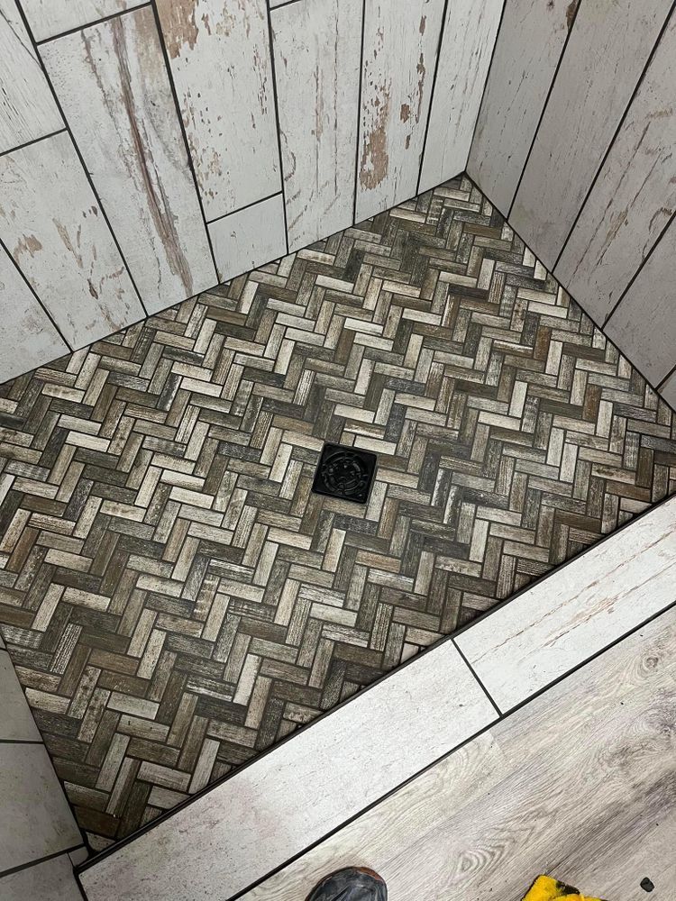 Small herringbone-tiled shower floor with a central drain, surrounded by white wood-paneled walls.