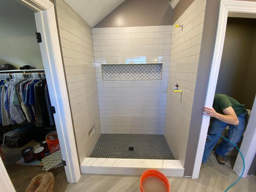 Partially tiled shower under construction with a recessed shelf and orange bucket in the foreground