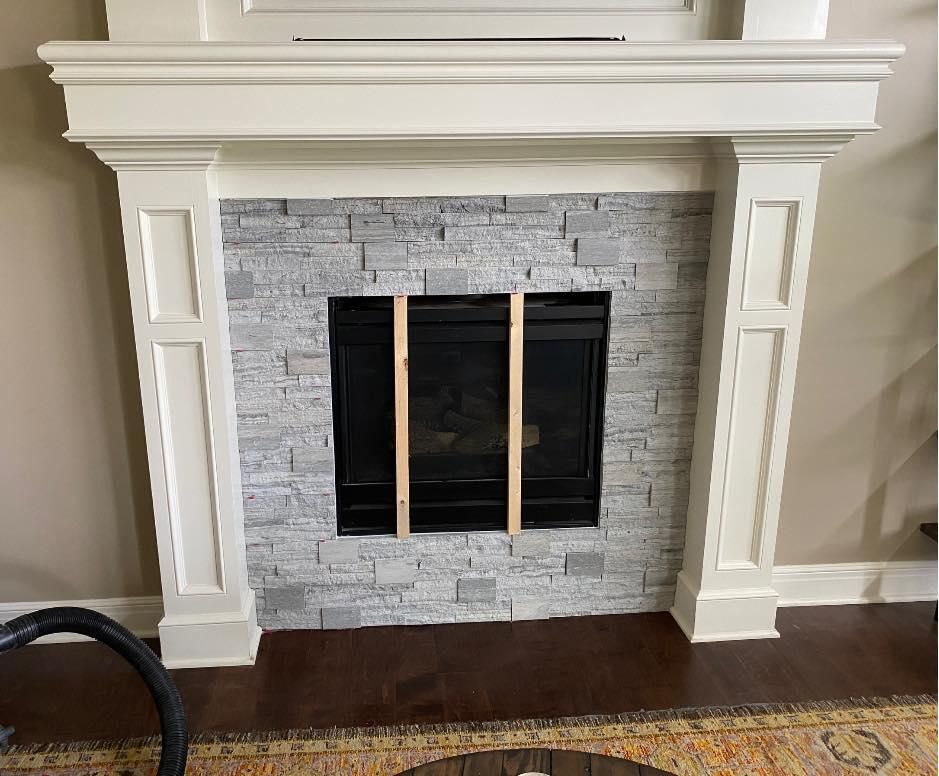 White fireplace with gray tile surround and black firebox, in a living room with hardwood floor.