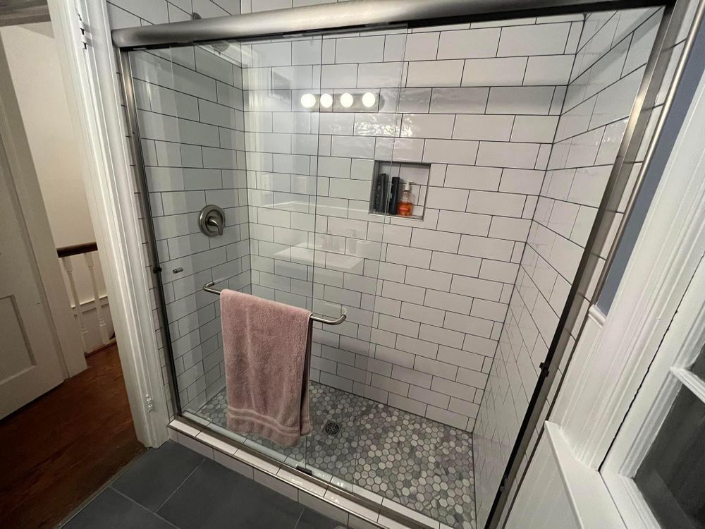 Glass-enclosed tiled shower with white subway tiles, pebble floor, and a pink towel hanging inside