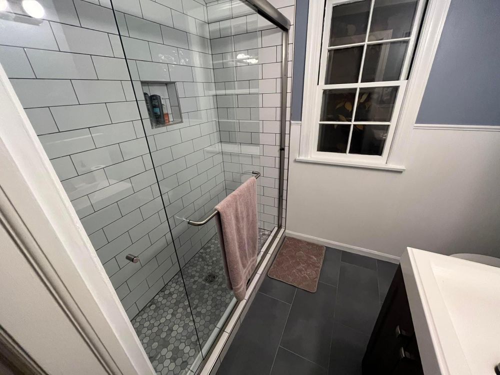Modern bathroom with glass walk-in shower, white subway tile, dark vanity, and a window above a pink towel on towel bar