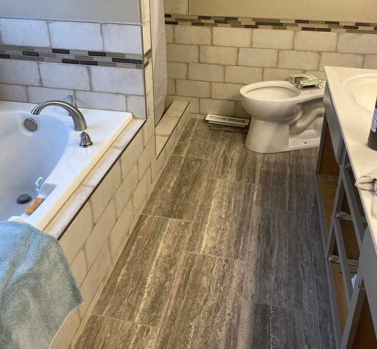 Bathroom with a bathtub, toilet, and vanity, featuring gray tile flooring and white subway-tile walls