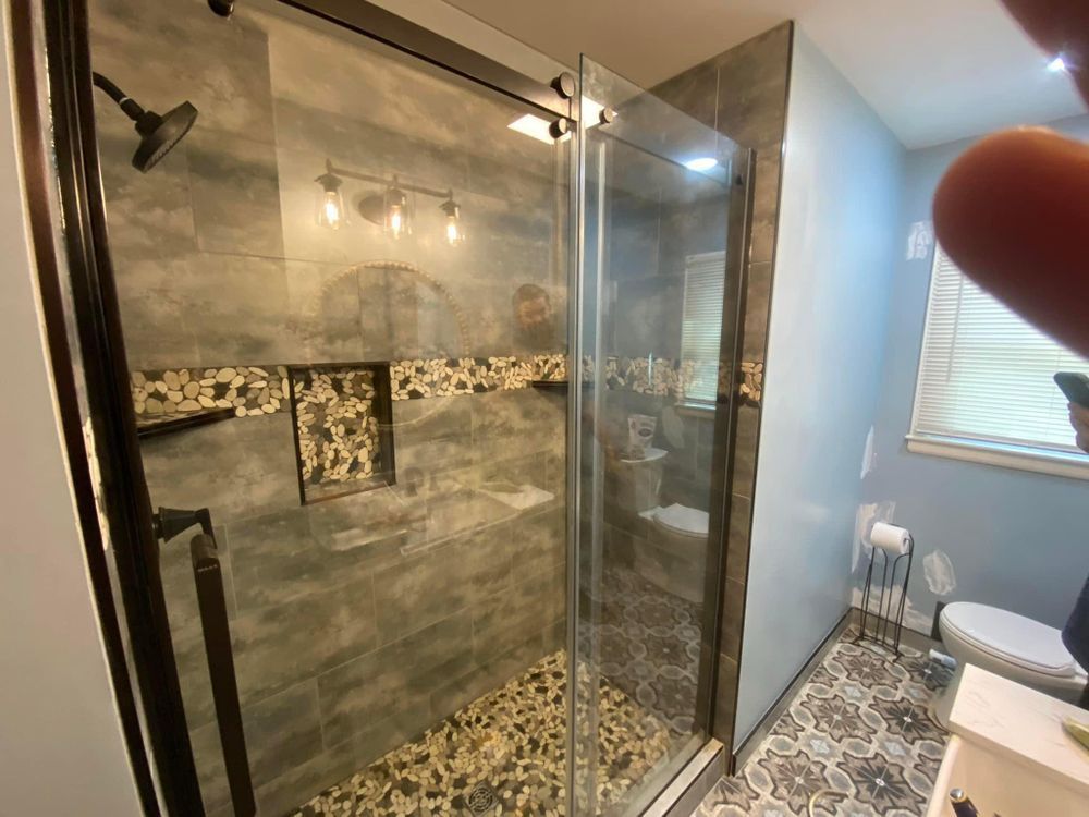 Modern walk-in shower with gray tile, pebble floor, glass door, and window beside toilet
