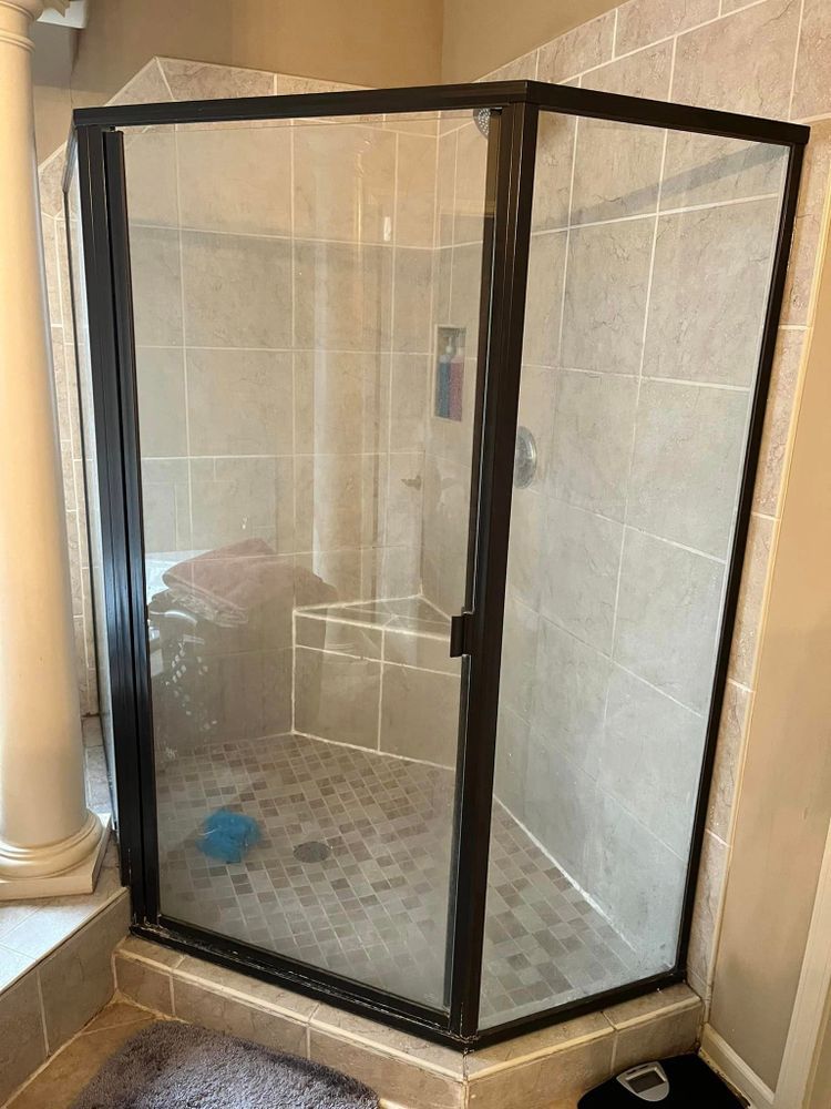 Corner glass shower enclosure with black frame and beige tiled walls in a bathroom