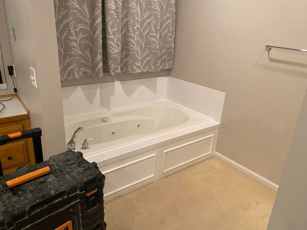 Bathroom with a white corner soaking tub, beige carpet, and gray patterned shower curtain