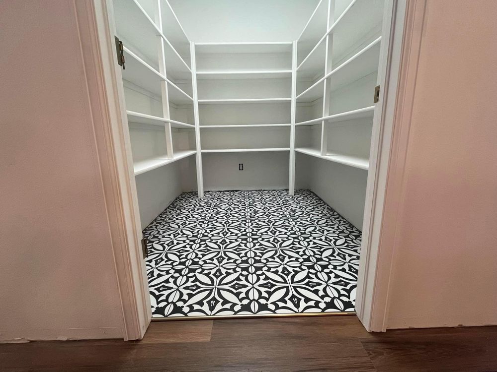 Empty walk-in closet with white shelves and patterned black-and-white tile floor.