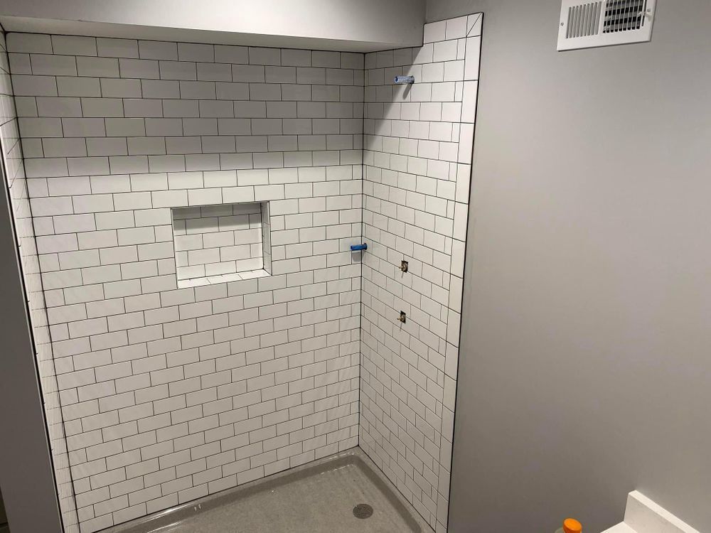 Empty tiled shower stall with gray walls, recessed niche, and drain in the floor