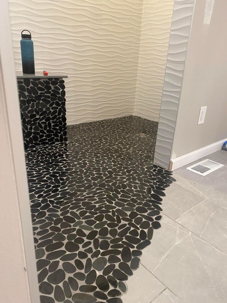 Small tiled alcove with a black pebble-pattern floor and a blue water bottle on a narrow ledge