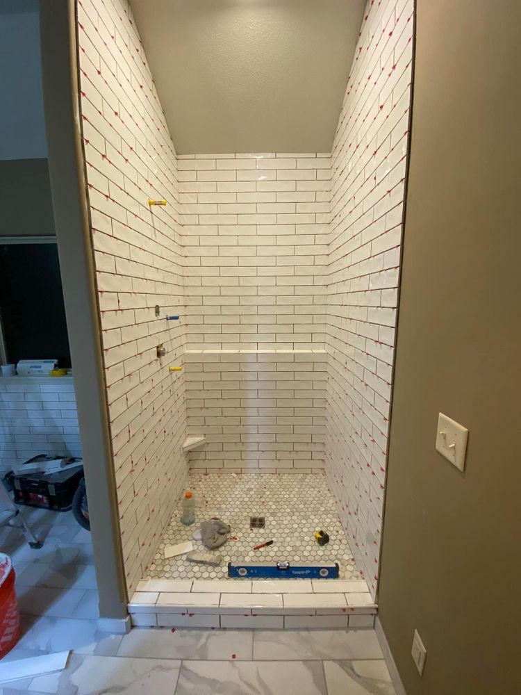Newly tiled walk-in shower under construction with white subway tile and a blue level on the floor