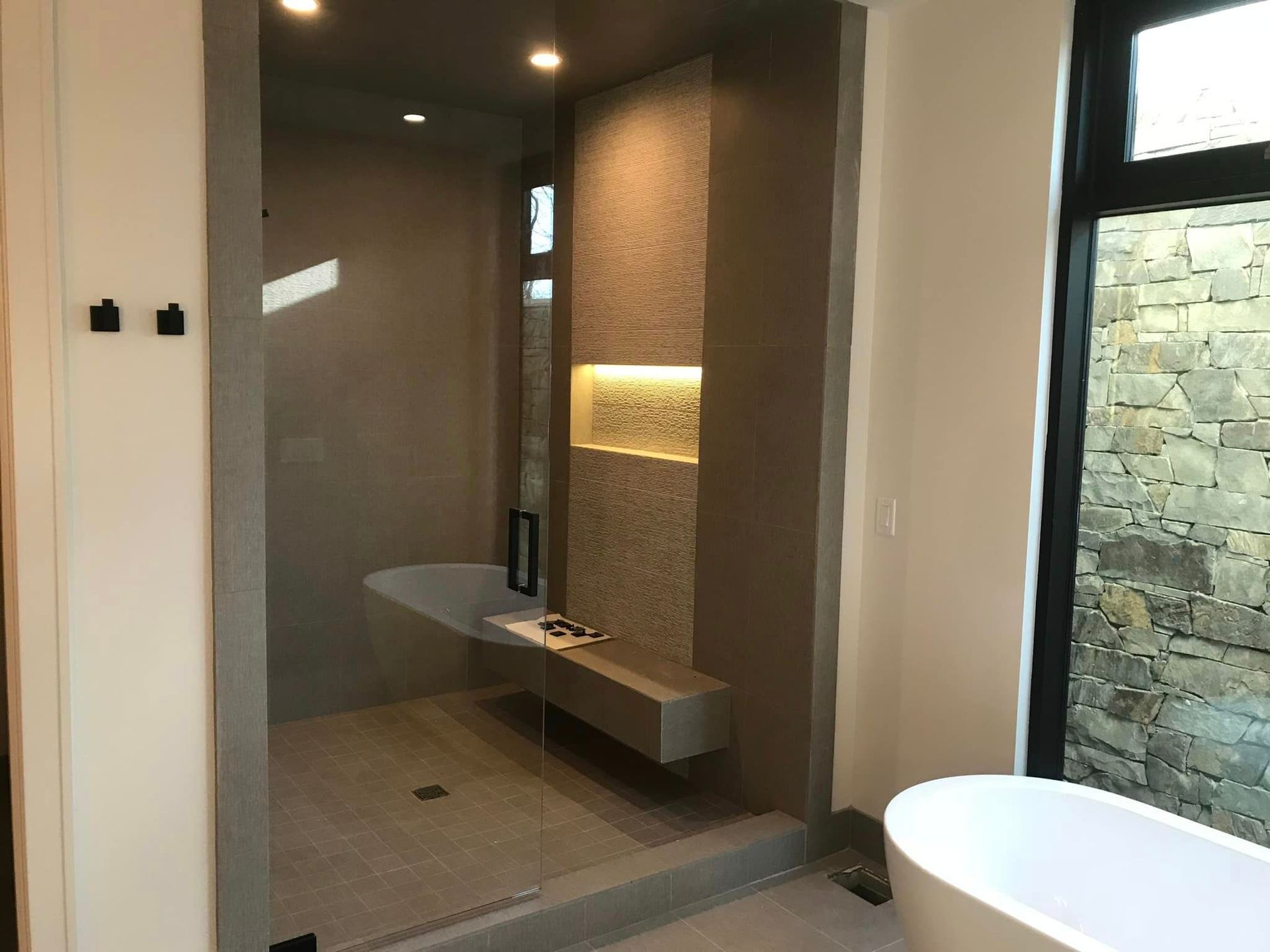 Modern bathroom with glass shower, stone accent wall, floating bench, and round white tub