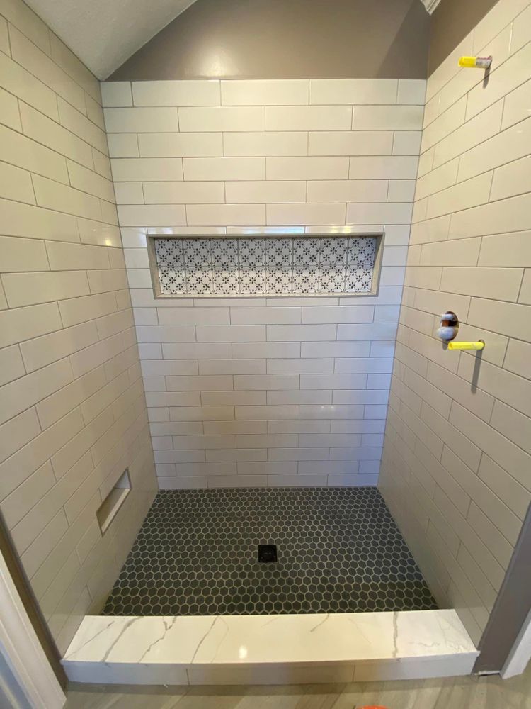 Empty tiled shower stall with a bench, mosaic floor, and small window opening.