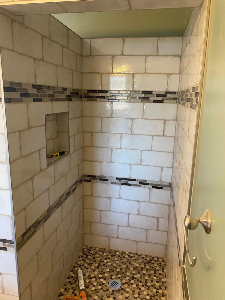 Small tiled shower stall with pebble floor and built-in wall niches, viewed through an open door