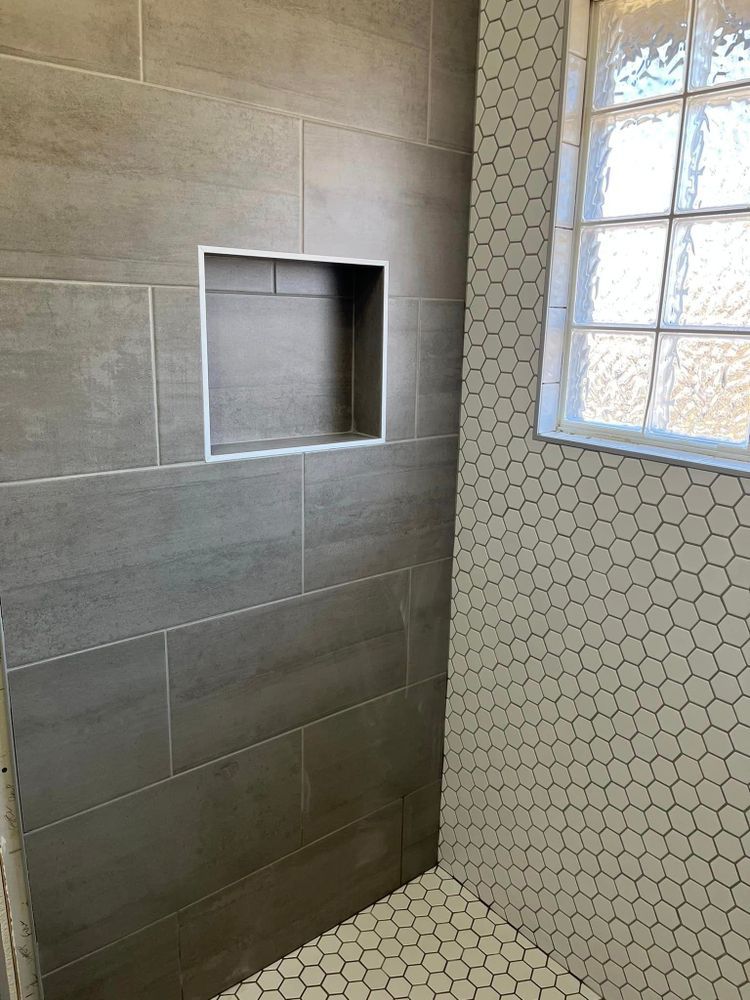 Tiled shower corner with a recessed shelf and hexagonal tile accent wall рядом to a window.