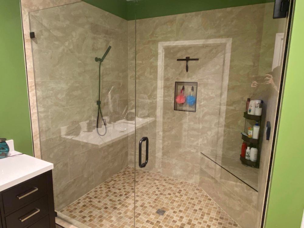 Glass walk-in shower with beige tile, built-in bench, shelf, and rainfall showerhead.