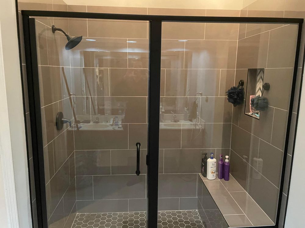 Glass shower with beige tile, black framed doors, and built-in shelves holding toiletries