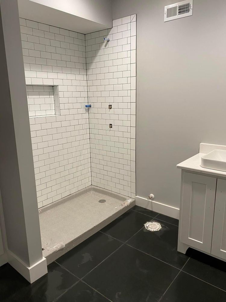 Modern bathroom with walk-in tiled shower, black floor tile, and white vanity