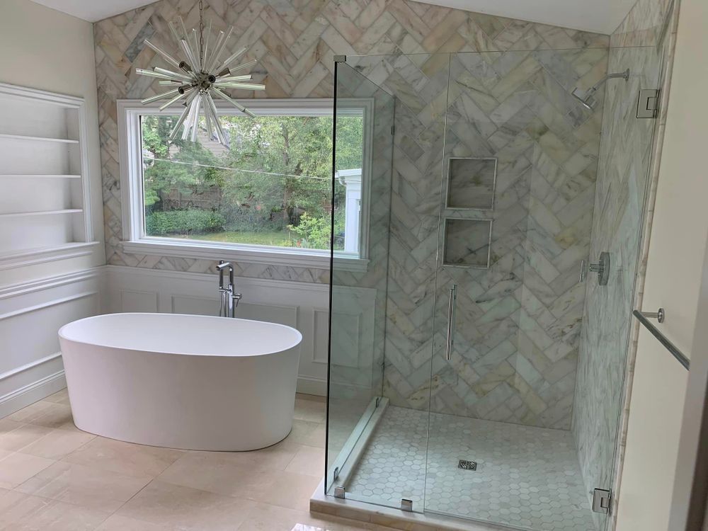 Modern bathroom with freestanding tub, glass shower, and marble tile walls beside a large window