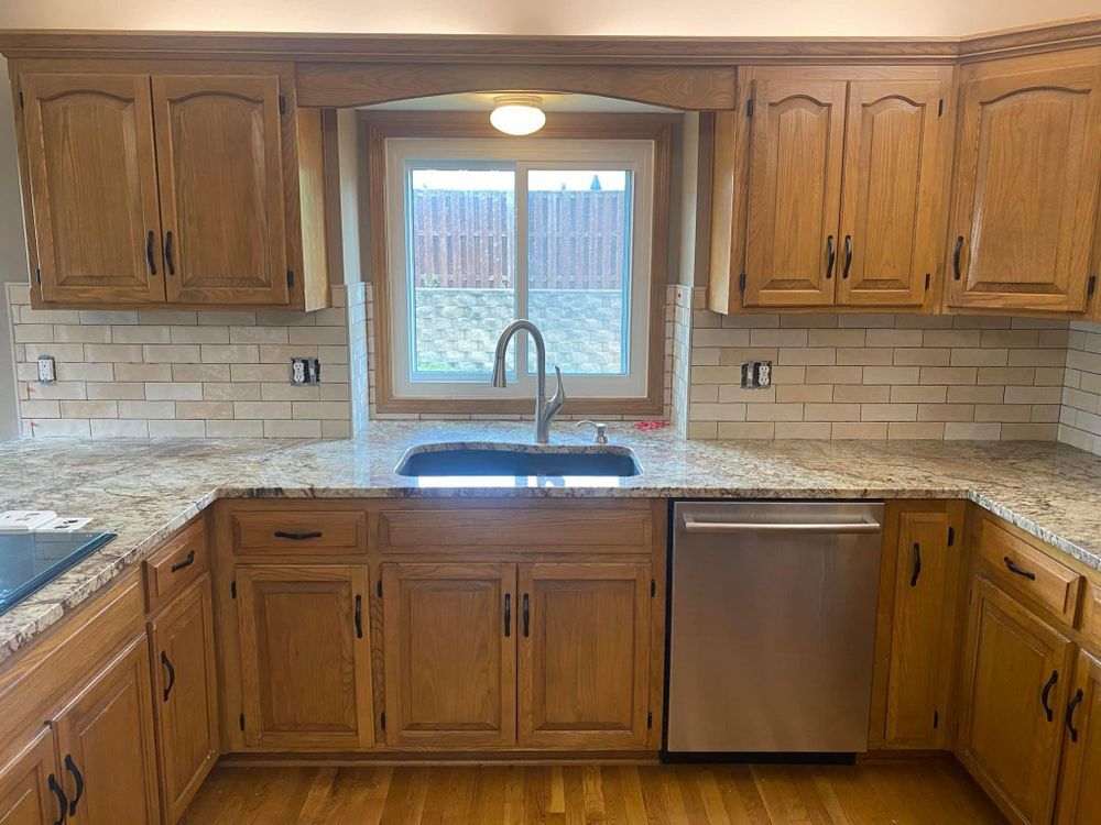 Empty kitchen with wooden cabinets, granite countertops, stainless dishwasher, and a window above the sink.
