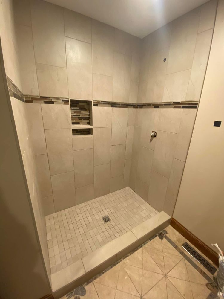 Walk-in tiled shower with built-in shelf, mosaic floor drain, and beige bathroom floor outside the threshold