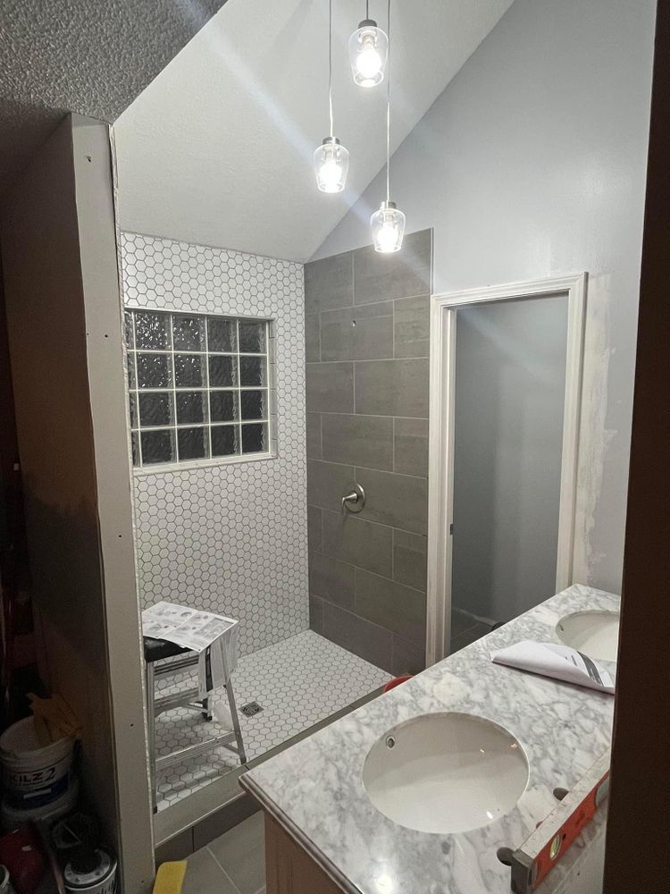 Modern bathroom with gray tile shower, glass wall, pendant lights, and marble vanity sink