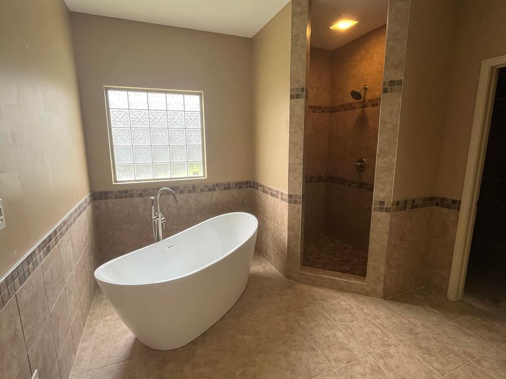 Modern bathroom with freestanding white tub, walk-in shower, and beige tile walls and floor