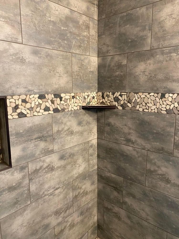 Corner of a tiled shower with a decorative mosaic band and small corner shelf