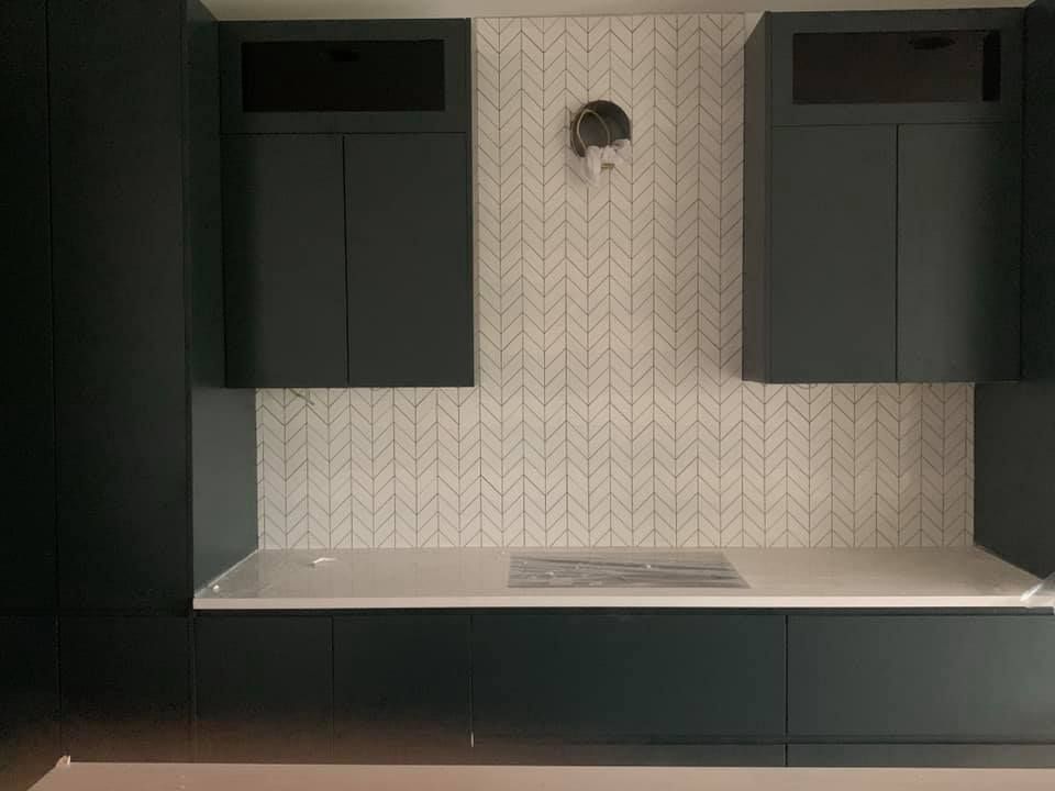 Modern kitchen wall with dark cabinets, white herringbone tile backsplash, and a white countertop.