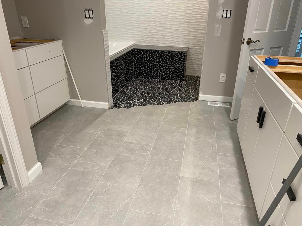 Modern kitchen with light gray tile floor, white cabinets, and a dark, pebble-tiled shower area ahead