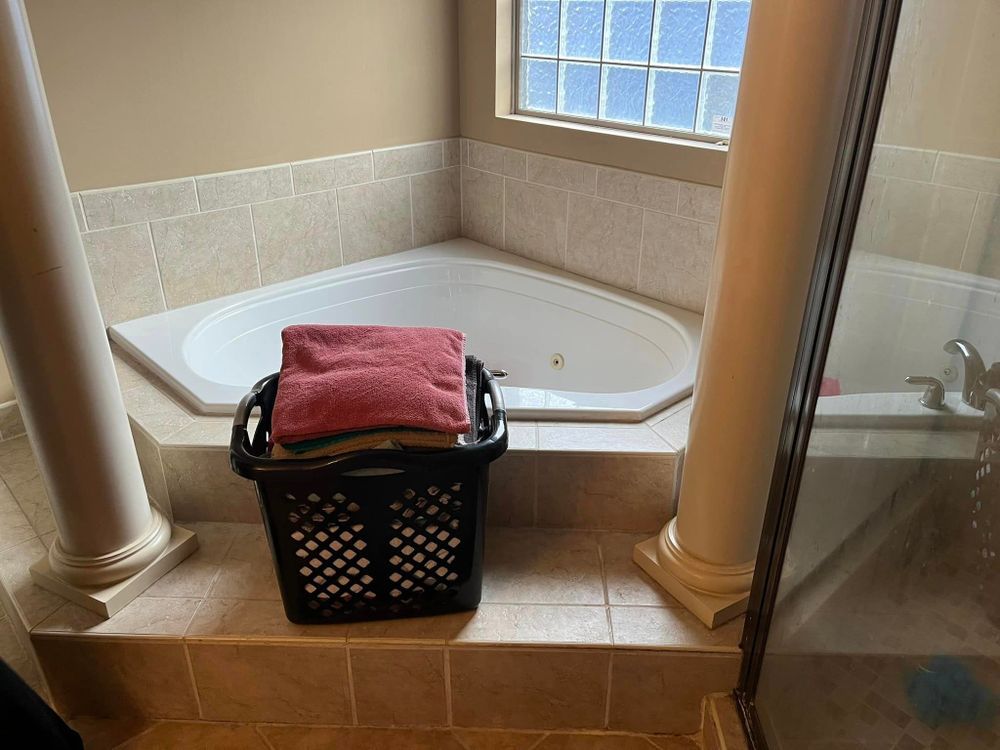 Bathroom with corner tub, tiled floor, window, and a laundry basket holding towels.