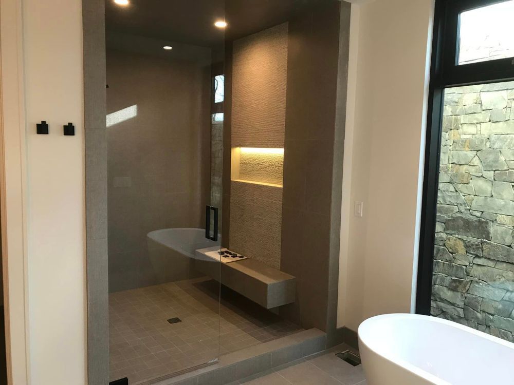 Modern bathroom with glass shower, floating vanity, and freestanding tub beside a stone wall.