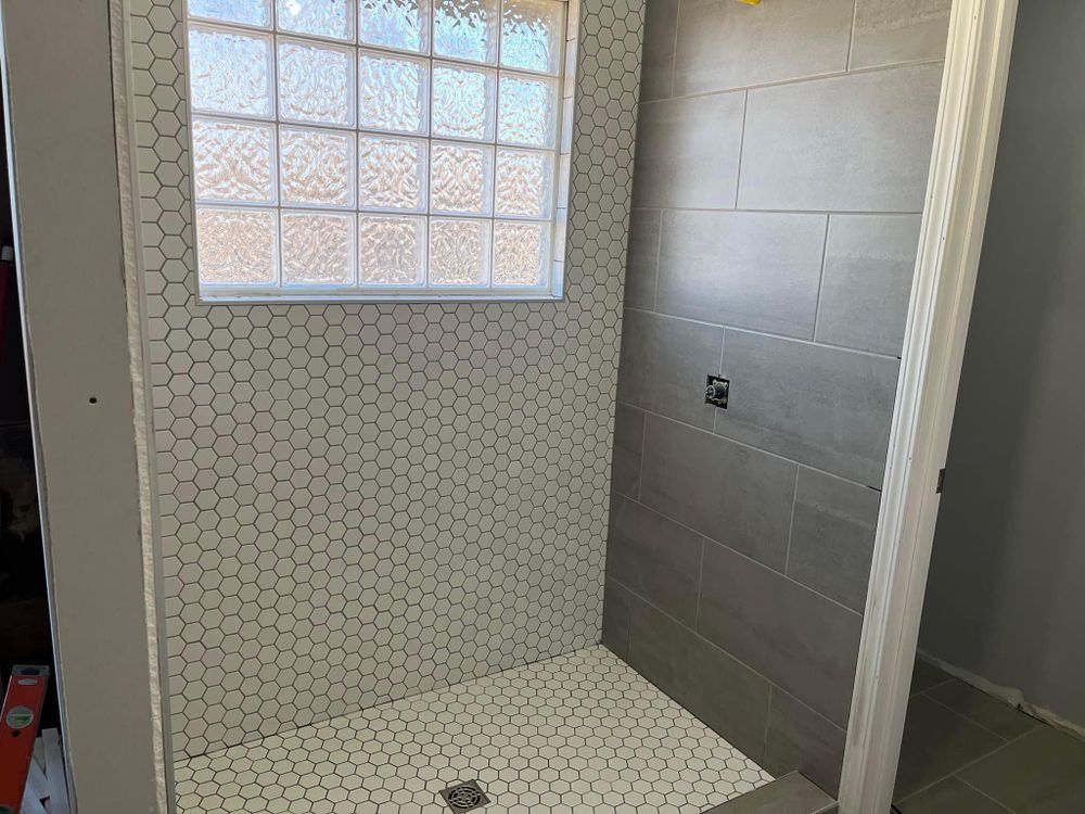 Tiled shower with a window, white mosaic wall, and gray side wall in a bathroom.